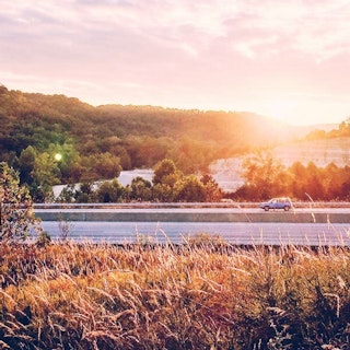 View of car on roadway with sunset in background